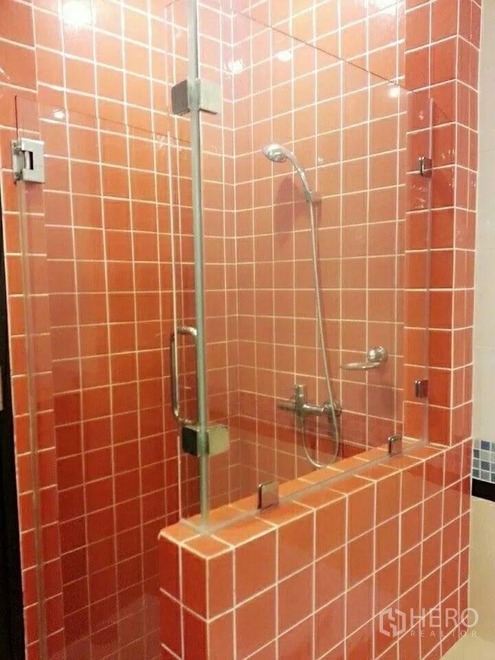 Condominium for rent in Khlong Toei, Bangkok - Glass-enclosed shower with orange tiles and handheld shower set.