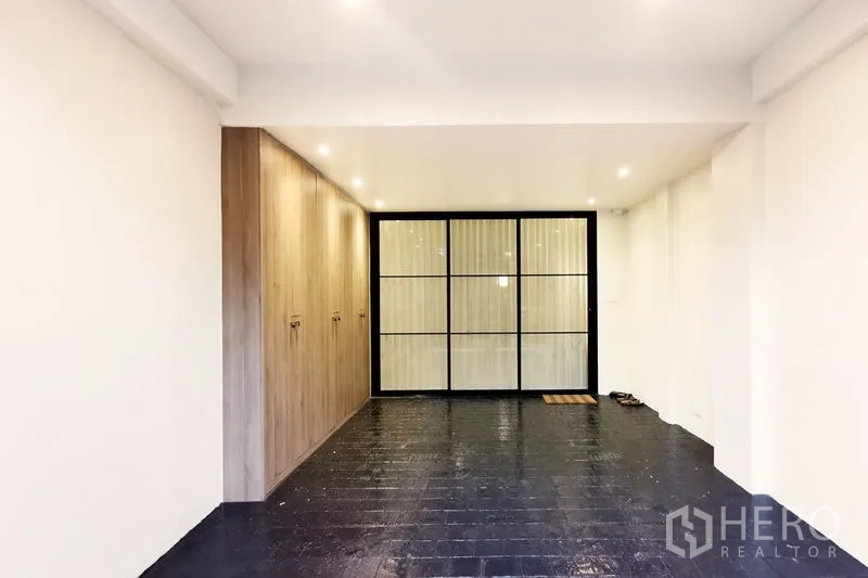 Townhouse for rent in Khlong Toei, Bangkok - Entrance garage area with built-in storage wall and black-framed glass partition doors.