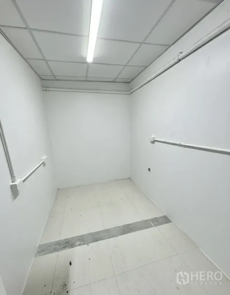 Retail Space for rent - Compact back room or storage area with white walls, ceiling light, and visible utility conduits.