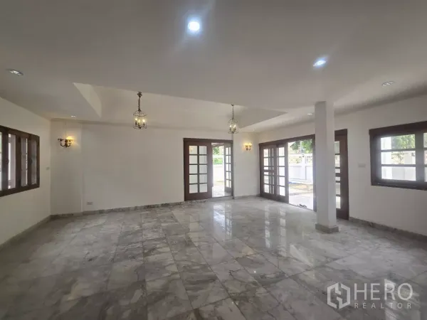 Detached House for rent in Phra Khanong, Bangkok - Open-plan living space with marble tiles, French doors to the patio and pendant lights.