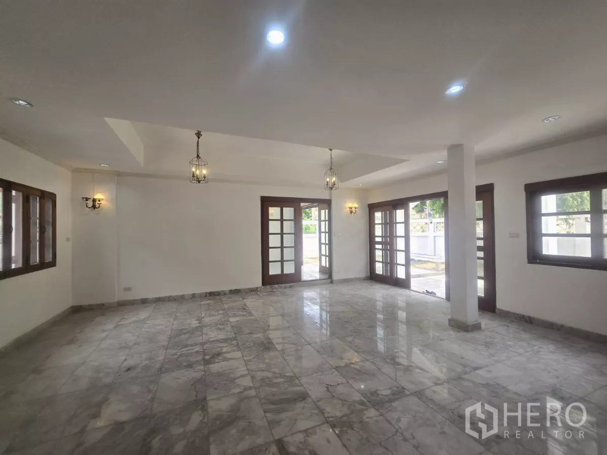 Detached House for rent in Phra Khanong, Bangkok - Open-plan living space with marble tiles, French doors to the patio and pendant lights.