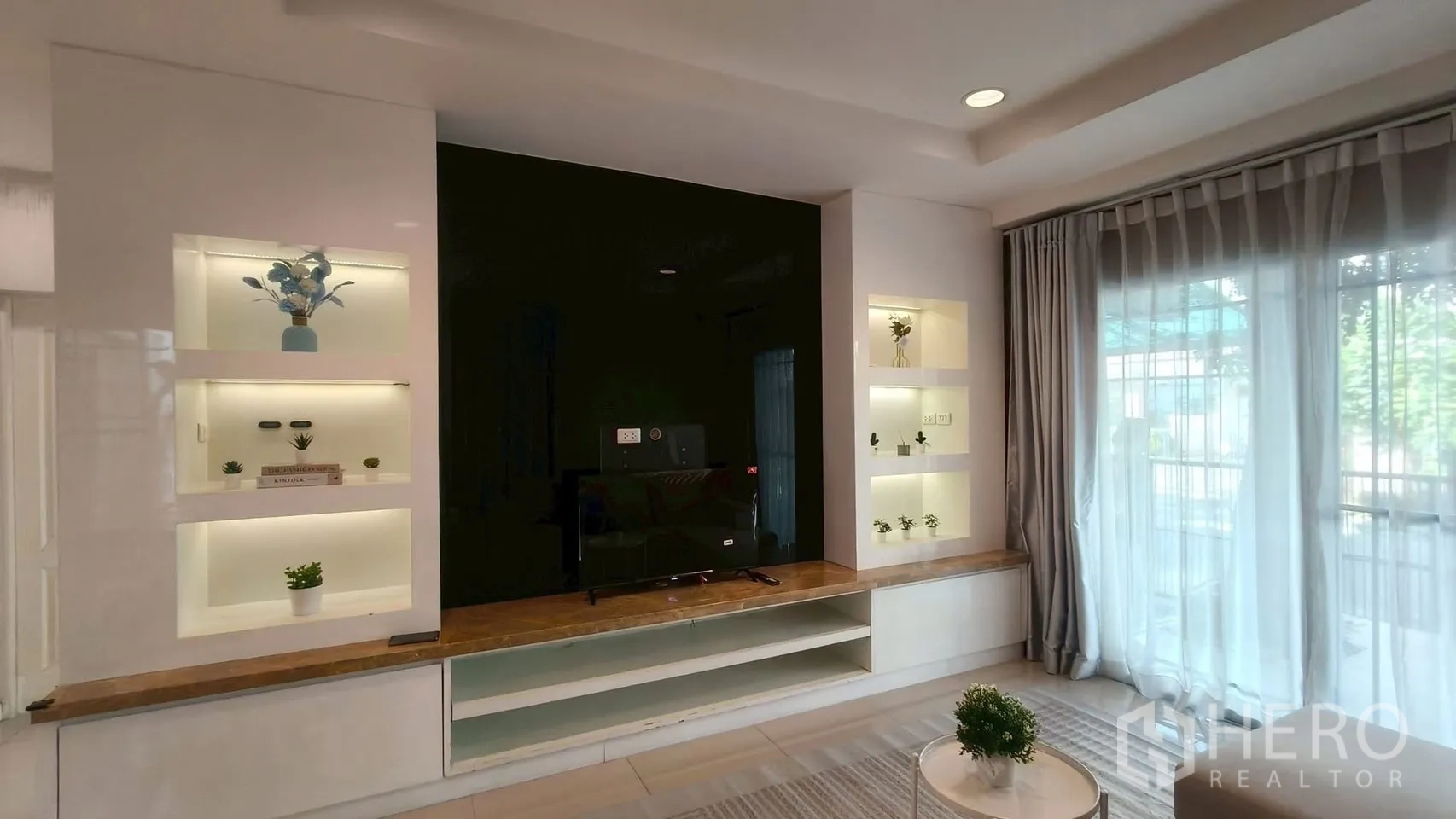 独立式住宅 出租或出售在Mueang Samut Prakan, Samut Prakan - 客厅电视背景墙，内置发光展示柜与推拉落地窗。