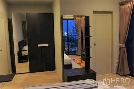Condominium for rent in Watthana, Bangkok - Bedroom suite with wardrobe and vanity mirror, doors to adjacent rooms, and curtain‑draped windows facing the city.