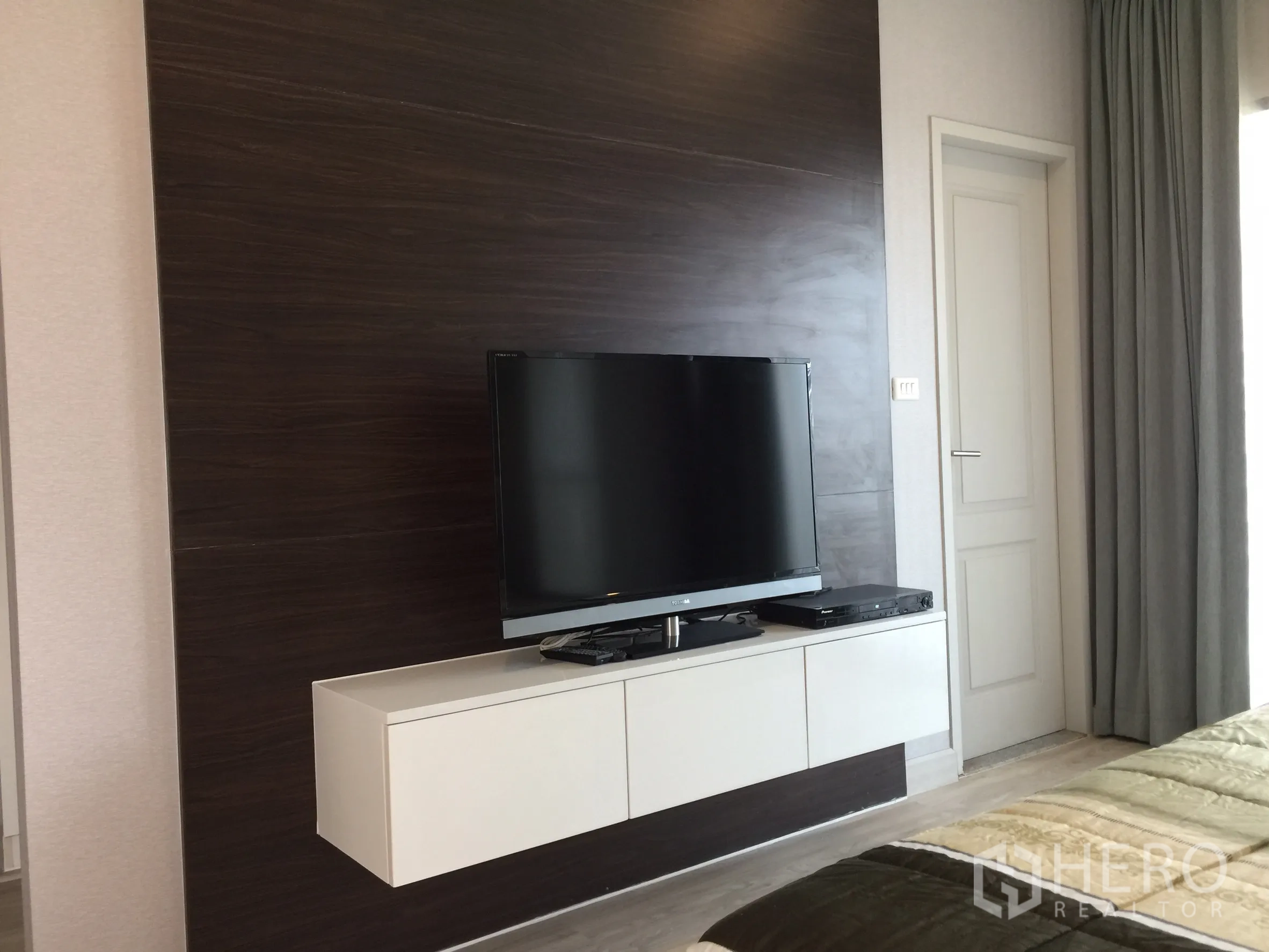 Condominium for rent or sale in Bangkok - Wall-mounted TV on a dark wood feature wall with floating console in the bedroom.
