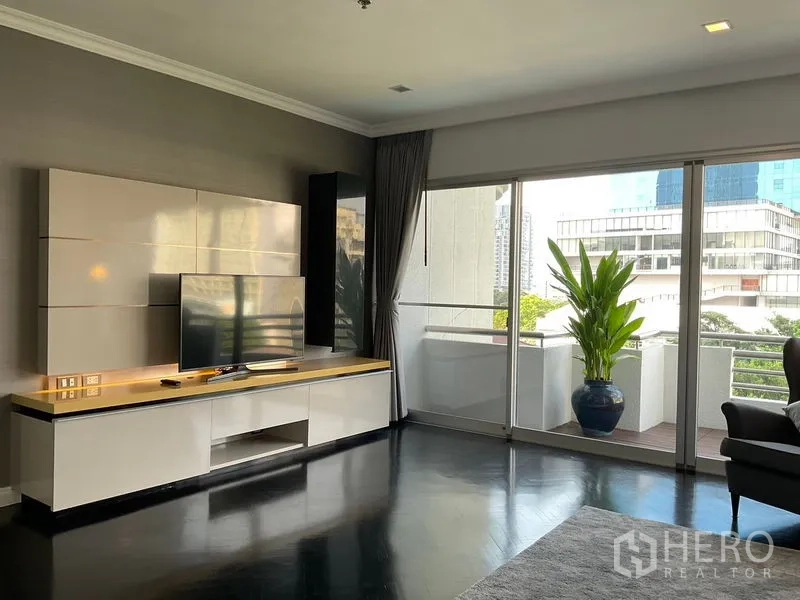 Apartment for rent in Sathon, Bangkok - Living room with TV console and sliding doors to a balcony with city views.