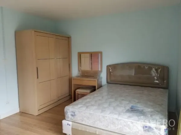 Townhouse for rent in Bang Kapi, Bangkok - Furnished bedroom with bed, wardrobe and dressing table against a soft blue wall.