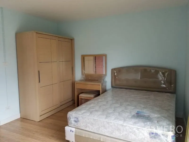 Townhouse for rent in Bang Kapi, Bangkok - Furnished bedroom with bed, wardrobe and dressing table against a soft blue wall.