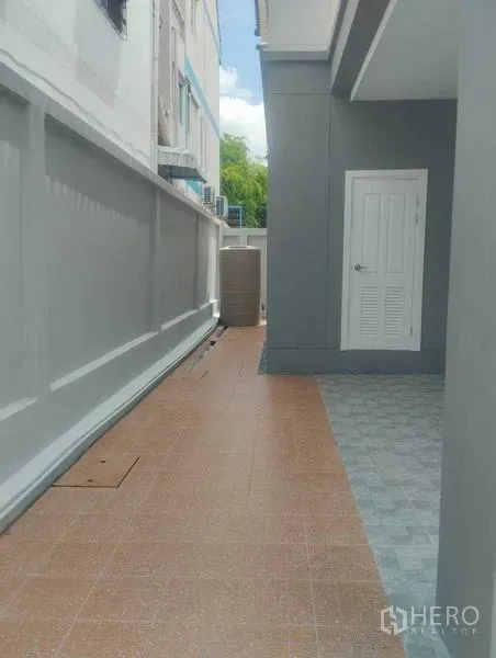 Detached House for sale in Phra Khanong, Bangkok - Tiled side walkway along the house with high boundary wall and a white utility door.