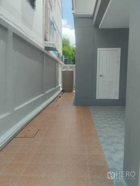 Detached House for sale in Phra Khanong, Bangkok - Tiled side walkway along the house with high boundary wall and a white utility door.
