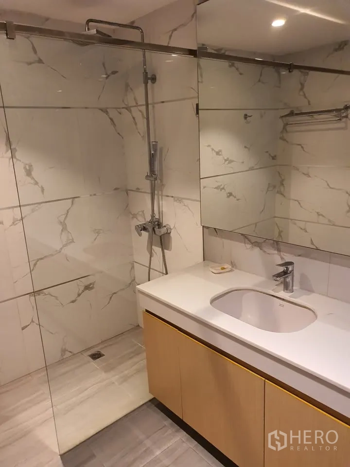 Condominium for rent in Watthana, Bangkok - Bathroom with glass shower enclosure, long vanity and marble-effect wall tiles.
