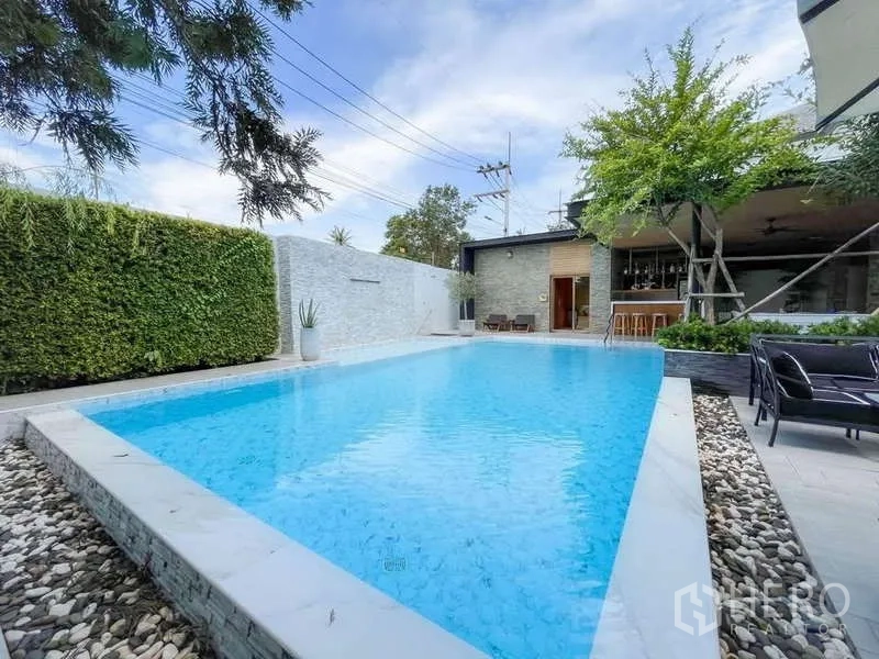 Detached House for sale in Bang Lamung, Chon Buri - Close view of the blue swimming pool with stone border, greenery and seating area.