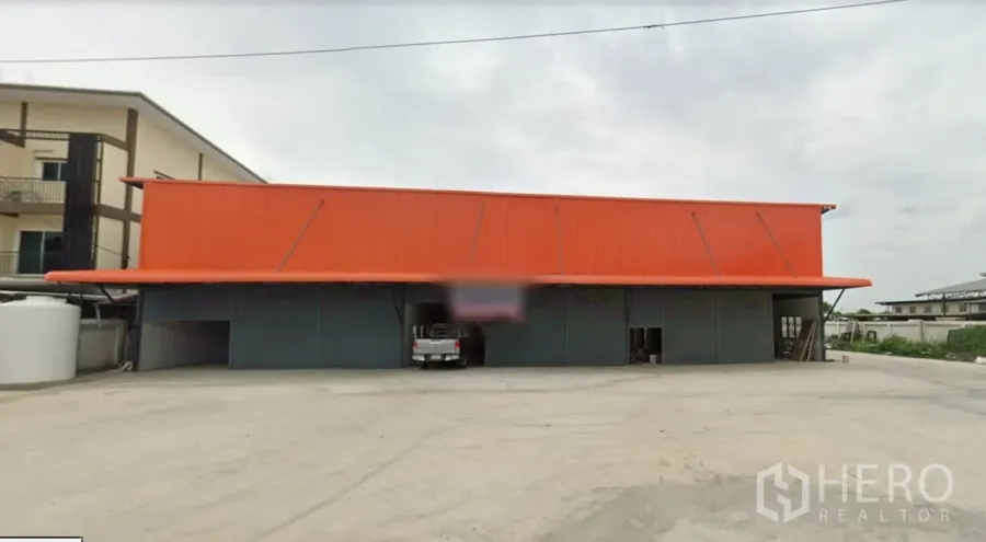 Warehouse for rent in Lam Luk Ka, Pathum Thani - Street-facing warehouse with orange metal roof, multiple roller shutters and a large concrete yard in Lam Luk Ka.