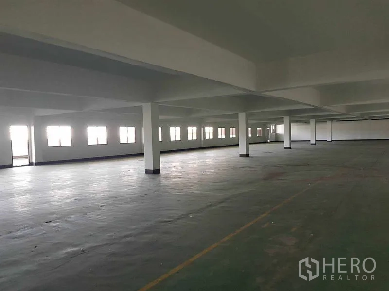 Warehouse for rent in Nong Khaem, Bangkok - Expansive industrial hall with long strip windows and marked concrete floor.