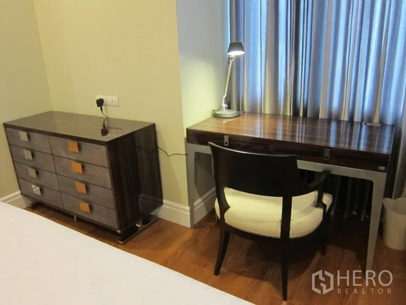 Condominium for rent in Khlong Toei, Bangkok - Close-up of study nook with wooden desk, chair and task lamp next to a drawer cabinet.
