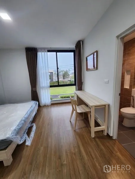 Townhouse for rent in Bang Phli, Samut Prakan - Bedroom with large window facing the garden, study desk, and access to an ensuite bathroom.