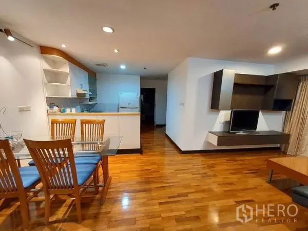 Condominium for rent or sale in Khlong Toei, Bangkok - Spacious open-plan area showing kitchen breakfast bar and mounted TV unit on wooden floors.