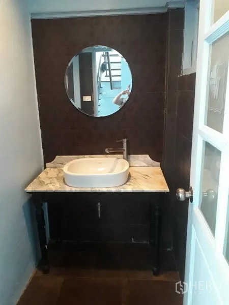 Detached House for rent in Watthana, Bangkok - Compact bathroom with round mirror and marble-top vanity.