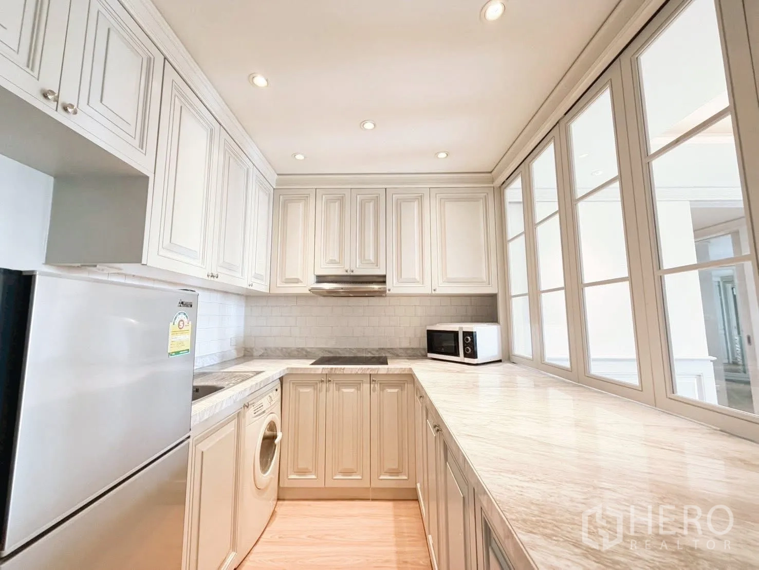 Condominium for rent or sale in Sathon, Bangkok - L-shaped kitchen with white cabinetry, fridge, cooktop, hood and washing machine.