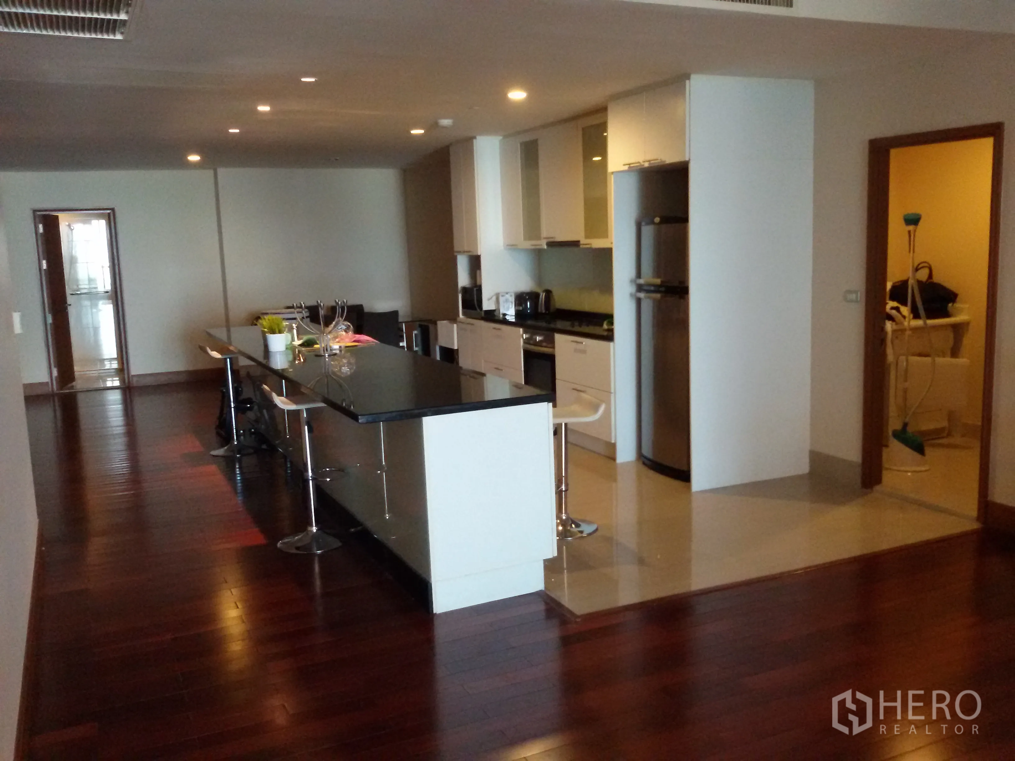 Condominium for rent in Sathon, Bangkok - Long kitchen island with bar stools beside an open living space and hardwood floors.