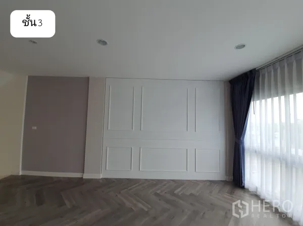 带办公室的家 出租或出售在Prawet, Bangkok - 三层客厅或会议区，白色墙面线条装饰、纱帘与深色鱼骨拼地板。