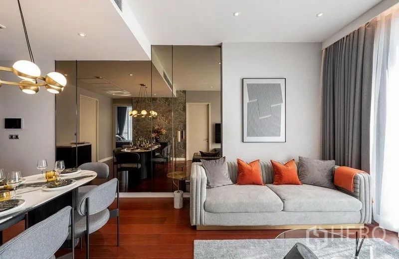 Condominium for rent in Watthana, Bangkok - Living room with mirrored feature wall, gray sofa with orange cushions, and view toward the dining area.