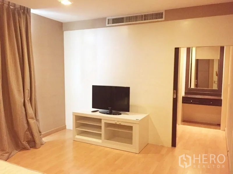 Condominium for rent in Khlong Toei, Bangkok - Bedroom lounge area with TV console leading to a dressing space.