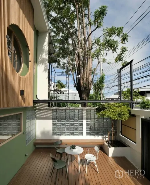 Townhouse for rent in Watthana, Bangkok - Private front courtyard with timber deck, built-in bench, outdoor dining set and a small tree beside a glass-block wall.