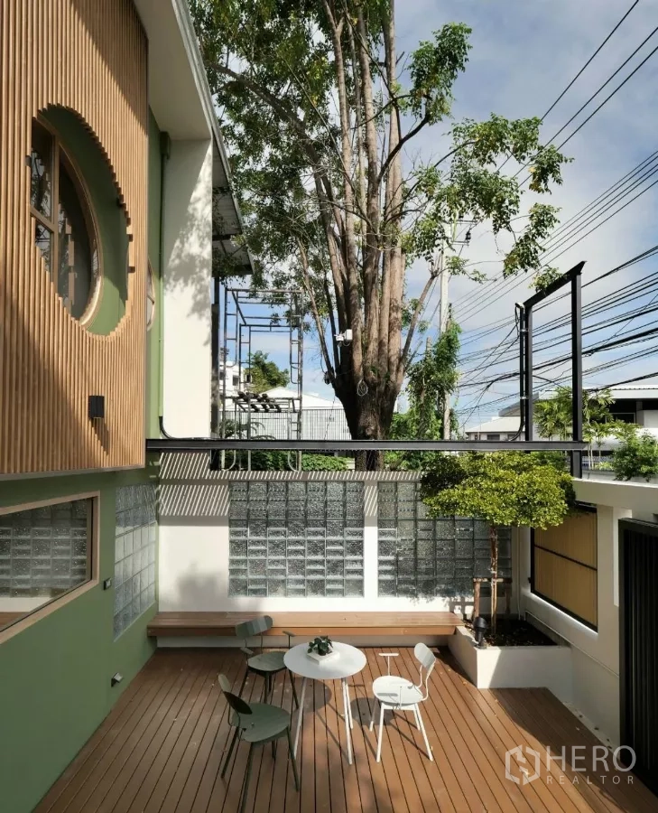 Townhouse for rent in Watthana, Bangkok - Private front courtyard with timber deck, built-in bench, outdoor dining set and a small tree beside a glass-block wall.