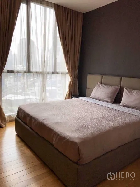 Condominium for rent in Watthana, Bangkok - Serene bedroom with large bed and floor-to-ceiling window offering city views.
