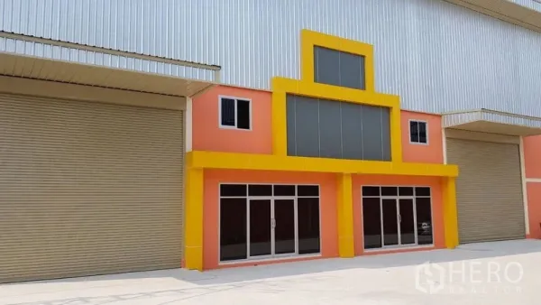 Warehouse for rent in Mueang Samut Prakan, Samut Prakan - Modern warehouse frontage with extra‑large roller shutter doors, a glass‑front office and a wide concrete driveway for loading.