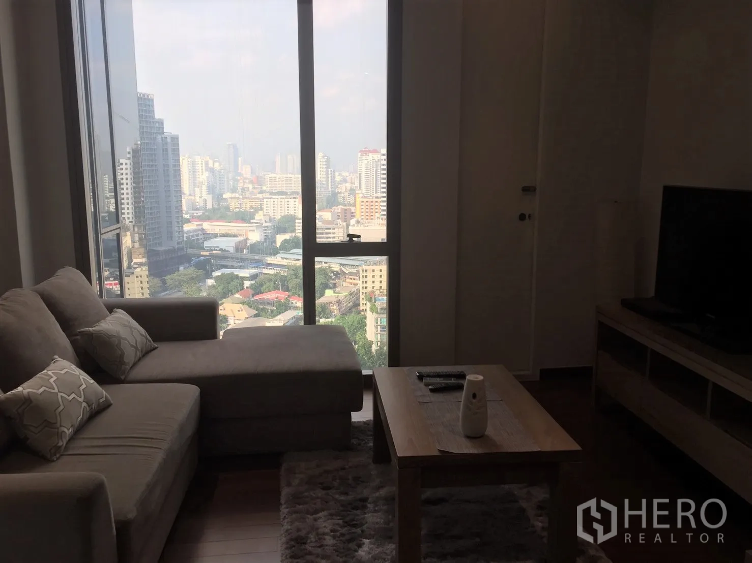 Condominium for rent in Khlong Toei, Bangkok - Cozy lounge with L-shaped sofa, coffee table and panoramic city view from a large window.