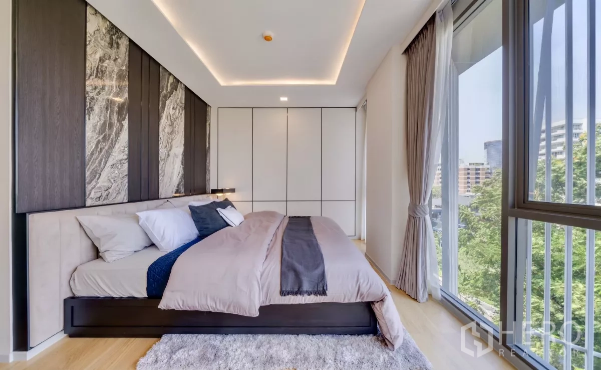 公寓 出租在Watthana, Bangkok - 主卧大床与通高玻璃窗，可观树梢景色。