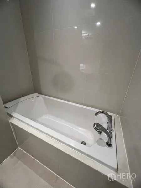 Condominium for rent in Khlong Toei, Bangkok - Close-up of a built-in soaking bathtub with chrome fixtures in a tiled bathroom.