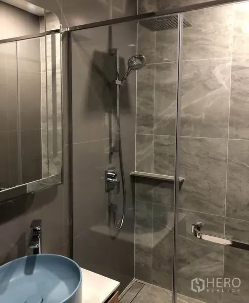 Condominium for rent in Watthana, Bangkok - Modern bathroom with a glass-enclosed shower, rain showerhead, and a blue vessel sink.