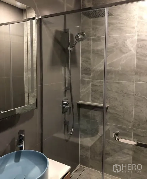 Condominium for rent in Watthana, Bangkok - Modern bathroom with a glass-enclosed shower, rain showerhead, and a blue vessel sink.