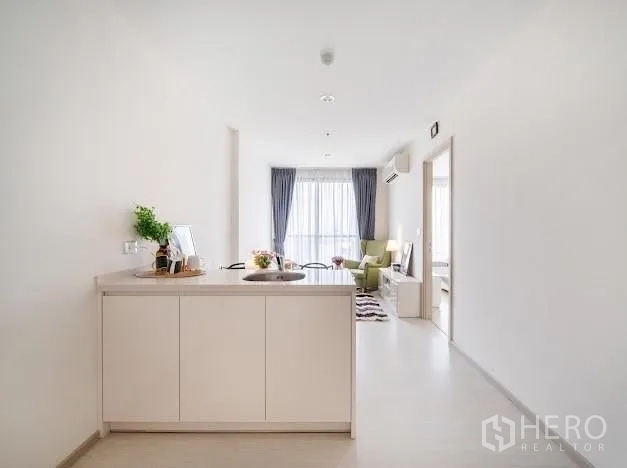 Condominium for sale in Khlong Toei, Bangkok - Long galley kitchen looking toward a sunlit living room and balcony window.
