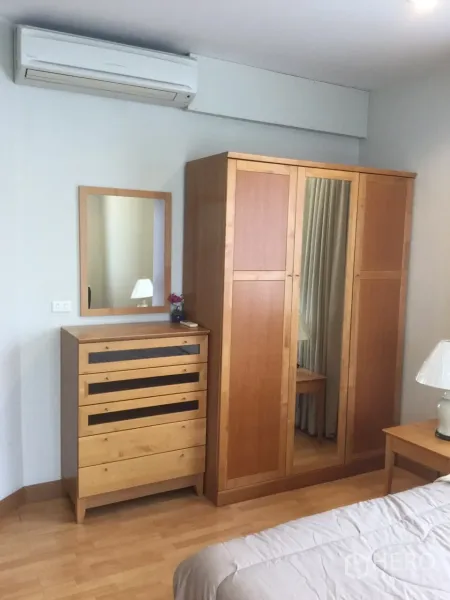 Condominium for rent in Khlong Toei, Bangkok - Bedroom corner with wooden wardrobe, dresser and wall-mounted air conditioner.