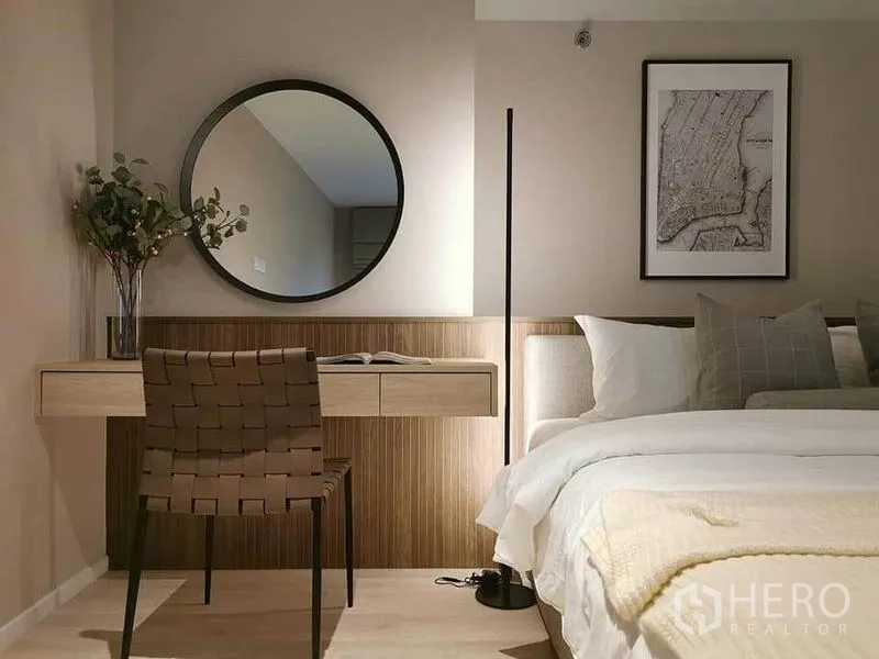 Condominium for rent in Bang Rak, Bangkok - Minimalist bedroom with soft lighting, built-in desk, round mirror and neatly made bed.