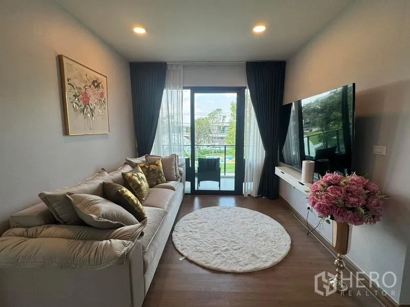 Detached House for rent or sale in Bang Phli, Samut Prakan - Cozy family room with sofa, TV wall and balcony access through a sliding door.