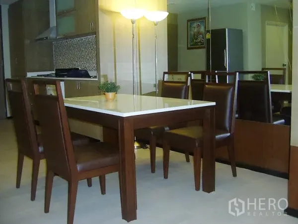 Condominium for rent in Khlong Toei, Bangkok - Dining area with six-seat wooden table beside modern kitchen, mirror wall and standing lamp in a Bangkok condo.