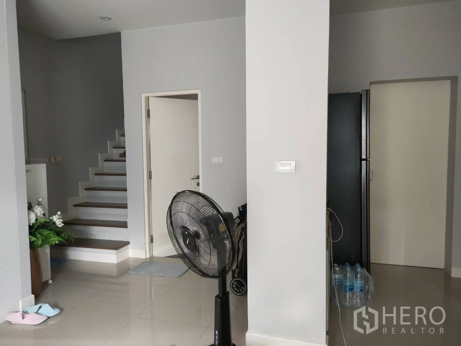 Detached House for rent or sale in Lam Luk Ka, Pathum Thani - Ground‑floor hallway showing staircase, doorways, glossy tiles, and a standing fan.