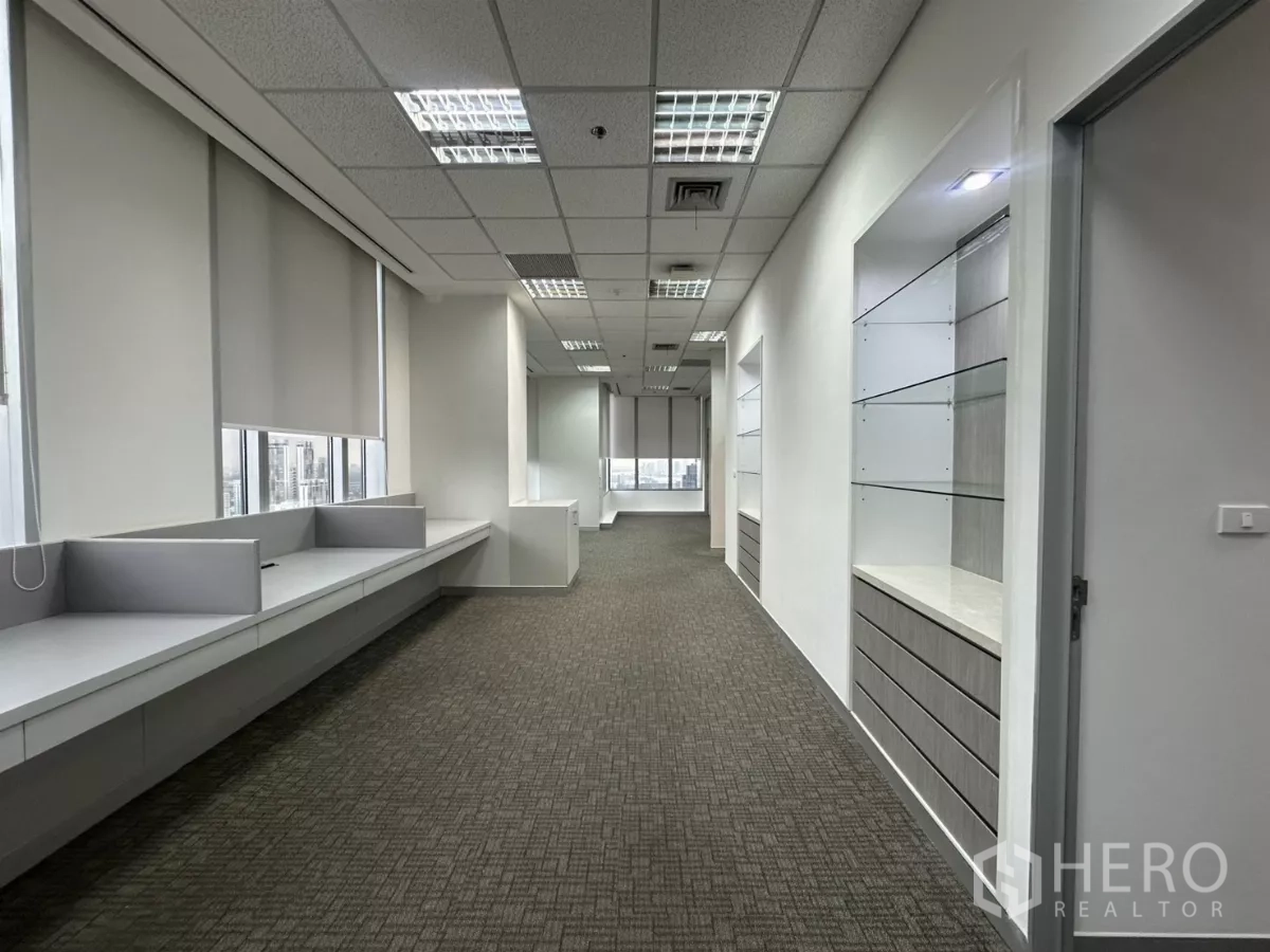 Office Space for rent in Watthana, Bangkok - Carpeted office corridor with built-in desks, window blinds and city views.