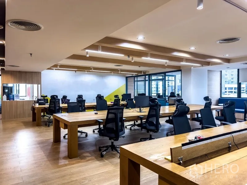 Office Space for rent in Bang Rak, Bangkok - Open workspace with long wooden benches, ergonomic chairs, and windows.