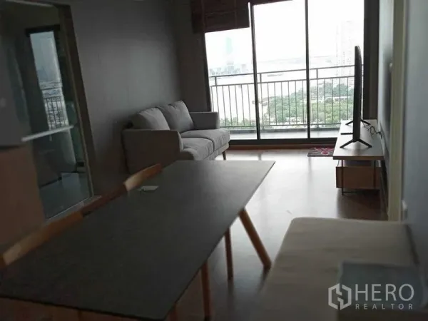 Condominium for rent in Yan Nawa, Bangkok - Open-plan living room with sofa, dining table and TV leading to a balcony with river view.