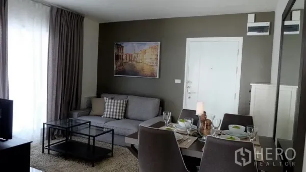 Condominium for sale in Khlong Toei, Bangkok - Wide view of the living room and dining table set beside full-height curtains.
