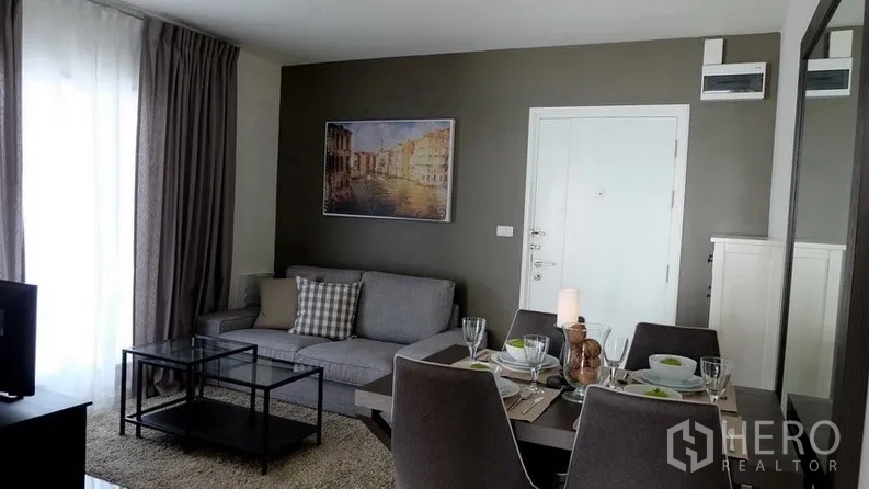 Condominium for sale in Khlong Toei, Bangkok - Wide view of the living room and dining table set beside full-height curtains.