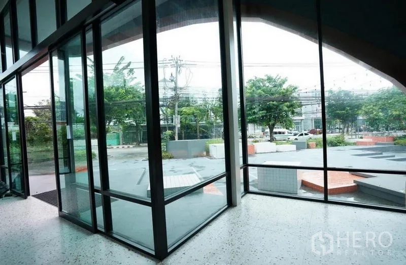 Standalone for rent in Bang Na, Bangkok - Interior glass corner looking out to the parking forecourt and trees.
