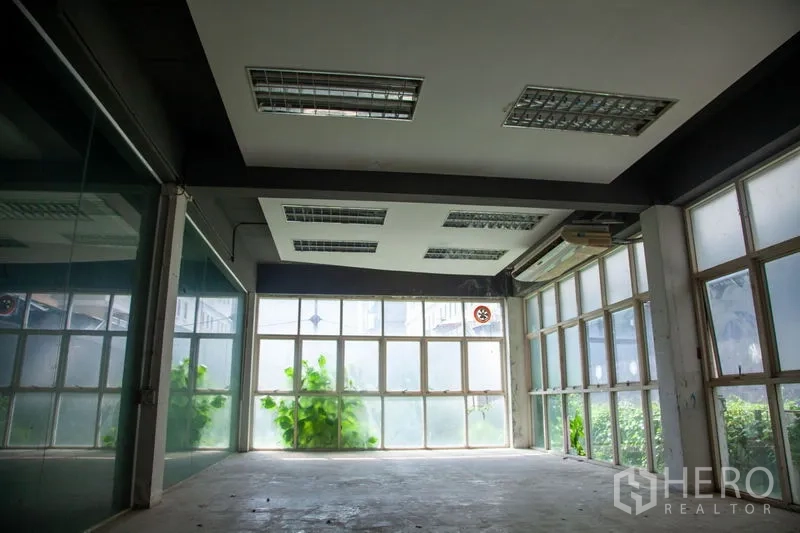 Warehouse for rent in Prawet, Bangkok - Ground-floor office or showroom with full-height windows, grid lighting and concrete floor inside the warehouse.