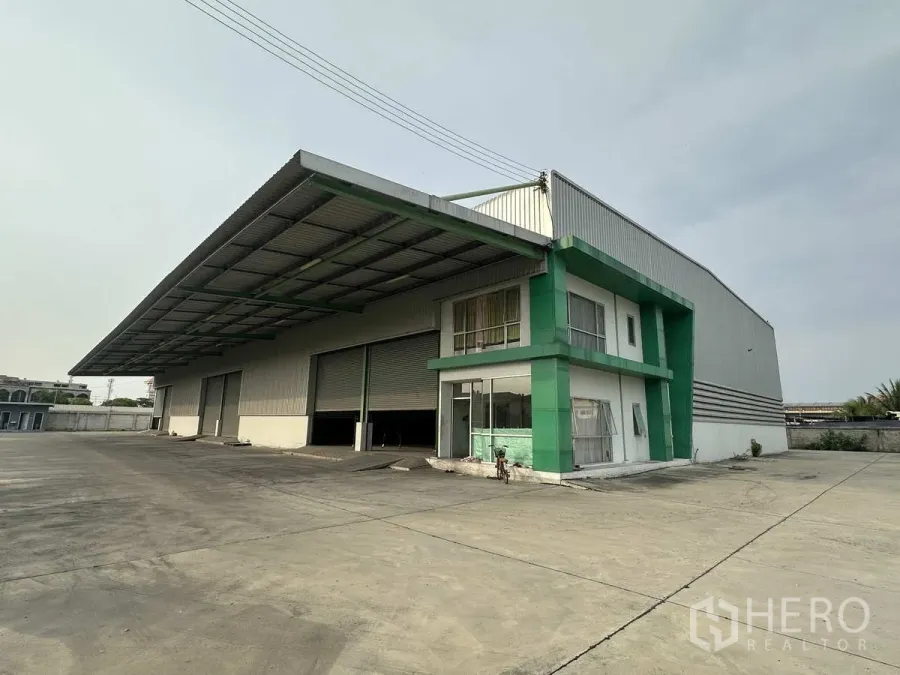 โรงงาน ให้เช่าในMueang Samut Prakan, Samut Prakan - อาคารโรงงานเดี่ยวพร้อมออฟฟิศกรอบสีเขียว กันสาดโหลดสินค้าขนาดใหญ่ ประตูม้วนหลายบาน และลานคอนกรีตกว้าง