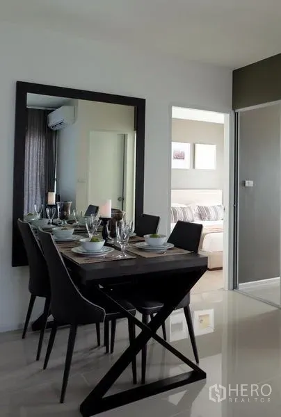 Condominium for sale in Khlong Toei, Bangkok - Contemporary dining area with large wall mirror and doorway leading to the bedroom.